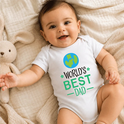 Baby wearing a 'World's Best Dad' onesie lying on a soft surface with a teddy bear.